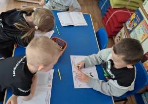 Grupa dzieci siedzi przy stoliku i koloruje książeczkę