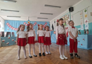 Dzieci stoją na środku sali i śpiewają piosenkę
