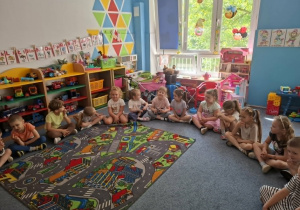 Dzieci siedzą na dywanie i wspólnie bawią się z panią prowadzącą