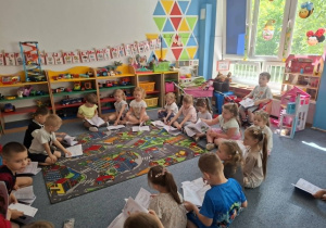 Dzieci siedzą na dywanie i oglądają książeczki