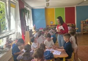 Dzieci siedzą przy stolikach i uzupełniają książki