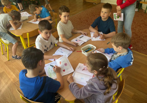 Dzieci siedzą przy stolikach i uzupełniają książki
