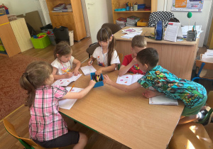 Dzieci siedzą przy stolikach i uzupełniają książki