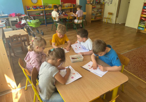 Dzieci siedzą przy stolikach i uzupełniają książki