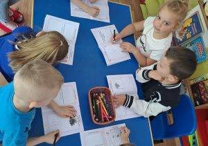 Grupa dzieci siedzi przy stole i rysuje w książeczkach