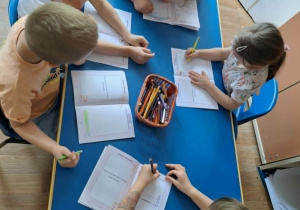 Grupa dzieci siedzi przy stole i rysuje w książeczkach