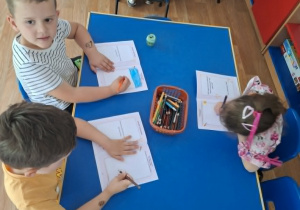 Grupa dzieci siedzi przy stole i rysuje w książeczkach