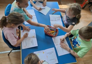 Grupa dzieci siedzi przy stole i rysuje w książeczkach