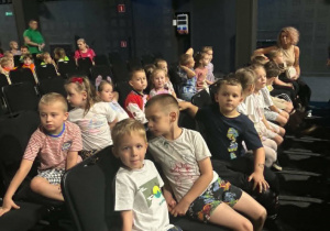 Grupa dzieci siedzi w teatrze na krzesłach i czeka na przedstawienie
