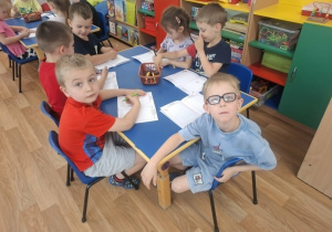 Grupa dzieci siedzi przy stoliku i koloruje książeczkę