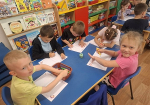Grupa dzieci siedzi przy stoliku i koloruje książeczkę