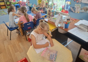 Dziewczynka siedzi przy stoliku i koloruje książeczkę