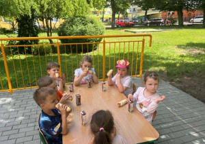 Dzieci jedzą hot-dogi na tarasie przedszkolnym