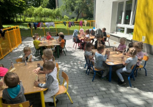 Dzieci jedzą hot-dogi na tarasie przedszkolnym