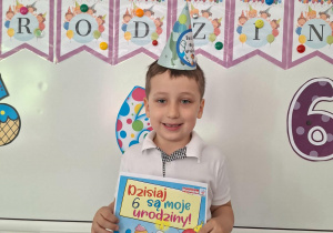 Damian stoi i pozuje do zdjęcia z urodzinowym dyplomem