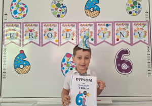 Damian stoi i pozuje do zdjęcia z urodzinowym dyplomem