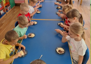Dzieci siedzą przy stole i spożywają lody