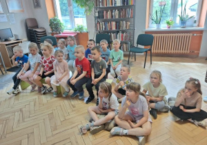 Dzieci siedzą i słuchają czytającej książkę p.bibliotekarki