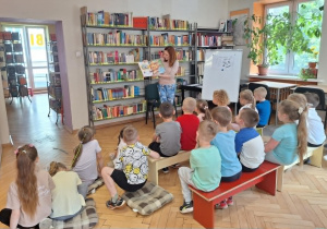 Dzieci siedzą i słuchają czytającej książkę p.bibliotekarki