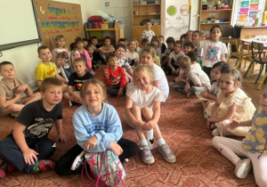 Przedszkolaki i uczniowie siedzą na dywanie