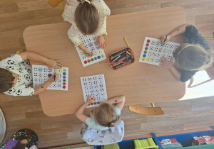Grupa dzieci siedzi przy stoliku i wykonuje pracę plastyczną