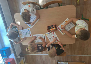 Grupa dzieci siedzi przy stoliku i wykonuje pracę plastyczną