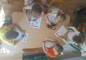 Grupa dzieci siedzi przy stoliku i wykonuje pracę plastyczną