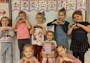 Marysia siedzi na krzesełku i pozuje do zdjęcia z dziewczynkami