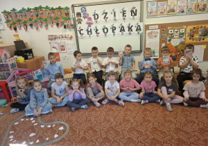 Dzieci pozują do zdjęcia na dywanie,chłopcy stoją a dziewczynki siedzą