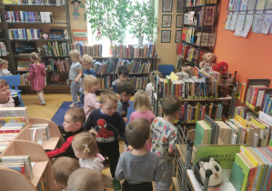 Dzieci szukają grzybków ukrytych między półkami w bibliotece