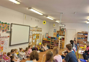 Dzieci siedzą na dywanie , studenci na krzesłach i wspólnie rozmawiają o higienie jamy ustnej