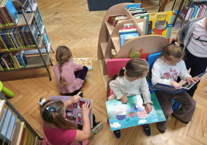 Grupa dzieci siedzi na krzesełkach i ogląda książki