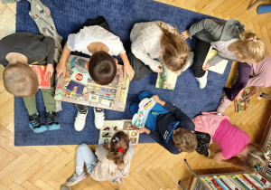 Grupa dzieci siedzi na dywanie i ogląda książki