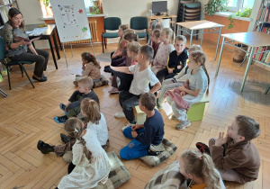Dzieci siedzą i słuchają jak pani bibliotekarka czyta im książkę