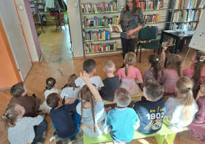 Dzieci siedzą i słuchają jak pani bibliotekarka czyta im książkę