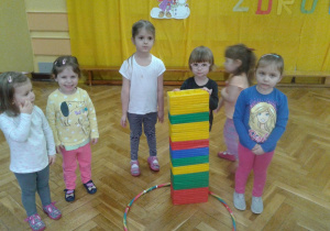 Dziewczynki z grupy młodszej stoją przy ustawionej przez siebie wieży z klocków