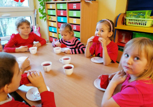Dzieci siedzą przy stole i jedzą czerwone ciasto