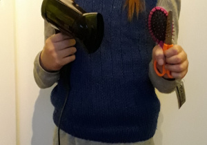 Dziewczynka trzyma w rękach suszarkę i szczotkę do włosów