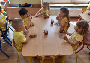 Dzieci spożywają przy stole żółty posiłek