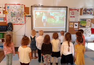 Grupa dzieci śpiewa hymn Polski w postawie na baczność