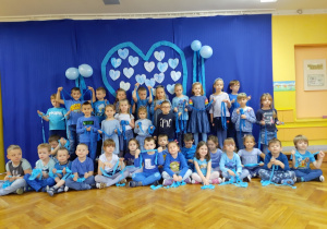 Dzieci ubrane na niebiesko pozują do zdjęcia na tle dekoracji - niebieskiego serca