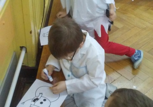 Trzech chłopców przykleja narysowanym bałwankom czarne kółeczka-guziczki