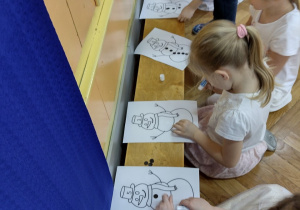 Dzieci przyklejają narysowanym bałwankom czarne kółeczka-guziczki