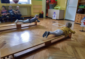 Dwie dziewczynki przeciągają się na ławkach leżąc na brzuchu