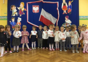 Dzieci śpiewają hymn Polski na tle dekoracji związanej z Narodowym Świętem Niepodległości