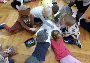 Grupa dzieci rysuje misia na dużym kartonie